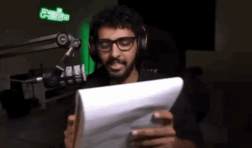 a man with glasses and headphones is reading a piece of paper in front of a microphone .