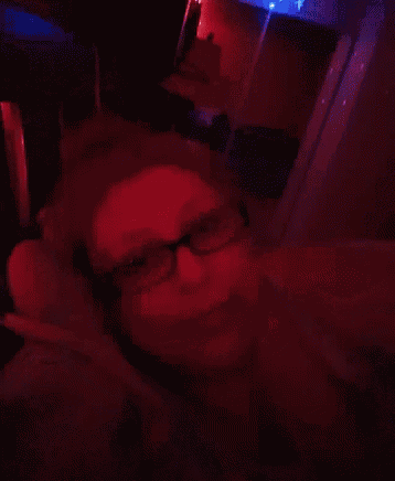 a person wearing glasses is laying in a dark room