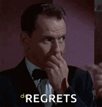 a man in a suit and tie is covering his mouth with his hand and the words `` regrets '' are behind him .