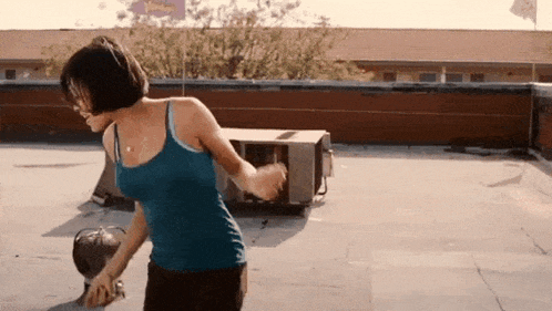 a woman in a blue tank top is dancing on the roof of a building