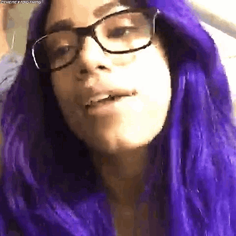 a woman with purple hair and glasses is wearing a purple wig .