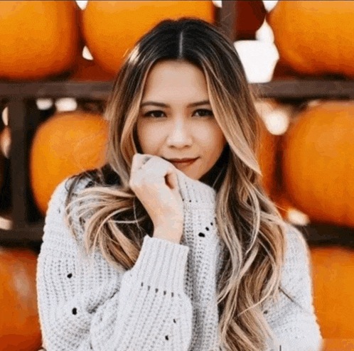 a woman wearing a sweater is standing in front of a pile of pumpkins
