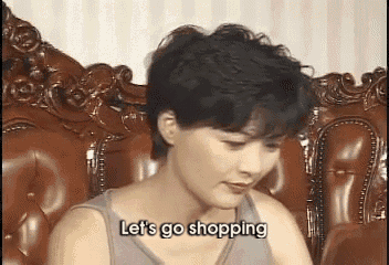 a woman is sitting on a couch with the words let 's go shopping written on her face .