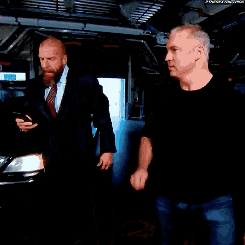 a man in a suit and tie stands next to another man in front of a car with the hashtag #thenextbigthing visible