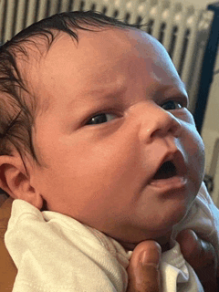 a person is holding a baby in their arms and the baby is looking at the camera .