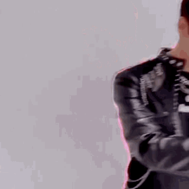 a man in a leather jacket is standing in front of a white wall and looking down .