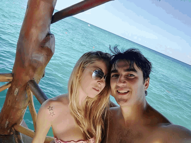 a man and a woman are posing for a picture in front of a body of water