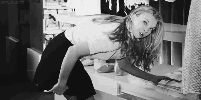 a woman in a white shirt and black skirt is reaching into a shelf .
