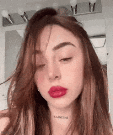 a woman with long brown hair and red lips is looking at the camera .