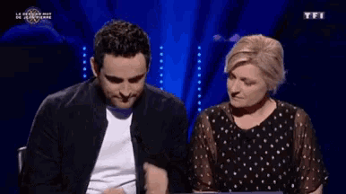 a man and a woman are sitting on a stage with tfi in the background
