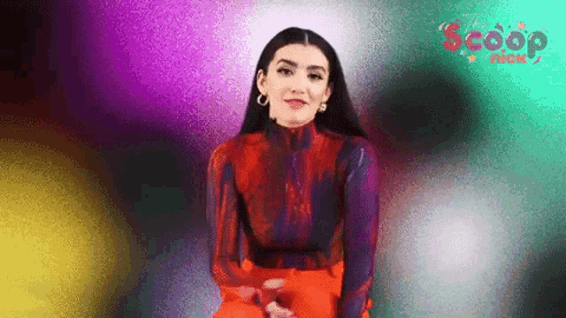 a woman in a red and purple top and orange pants is sitting in front of a multicolored background .