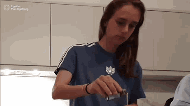 a woman in a blue adidas shirt is pouring something into a container
