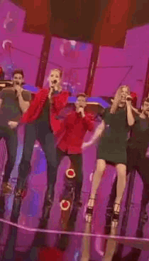 a group of people singing into microphones on a stage with a purple background