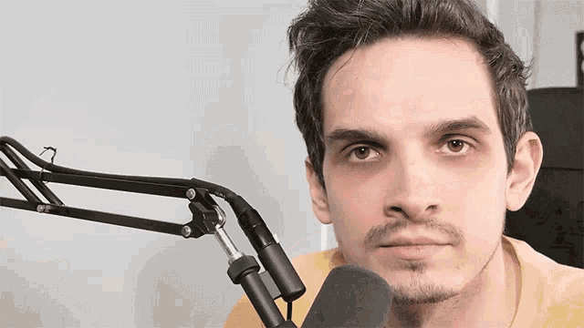 a man in a yellow shirt is sitting in front of a microphone and looking at the camera
