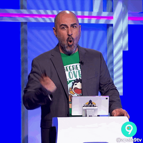 a man wearing a secret love shirt stands in front of a computer