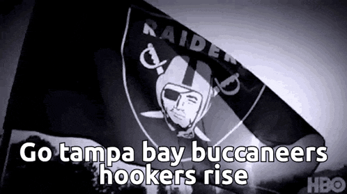 a raiders flag is flying in the wind with the words `` go tampa bay buccaneers hookers rise '' written on it .