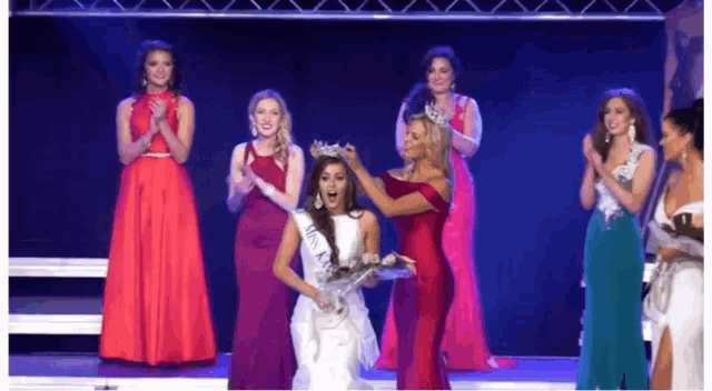a group of women are standing on a stage with one woman wearing a crown on her head .