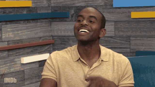 a man in a yellow shirt is laughing in front of a wall with imdb written on it