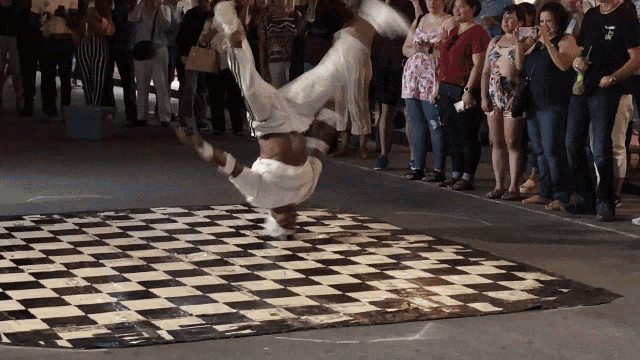 a man doing a handstand on a checkered floor in front of a crowd
