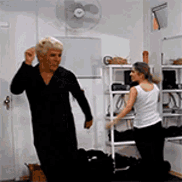 a man and a woman are dancing in a room with a fan on the wall