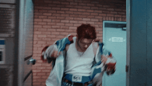 a man with red hair is standing in front of a brick wall and a door that says escape
