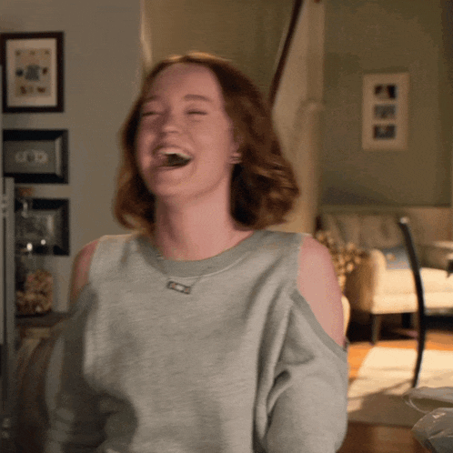 a woman wearing a grey off the shoulder sweater laughs