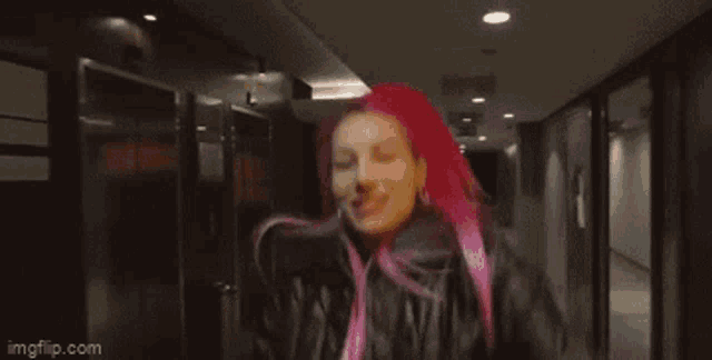 a woman with pink hair is dancing in a hallway while wearing a leather jacket .