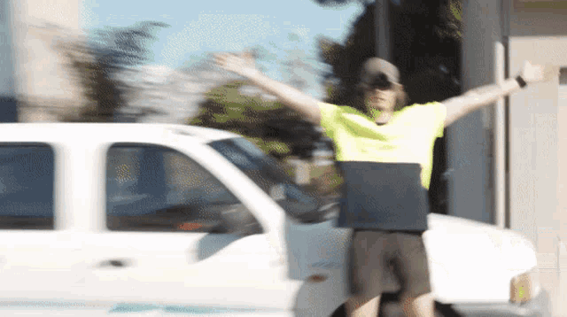 a man in a yellow shirt is standing in front of a white truck with his arms outstretched