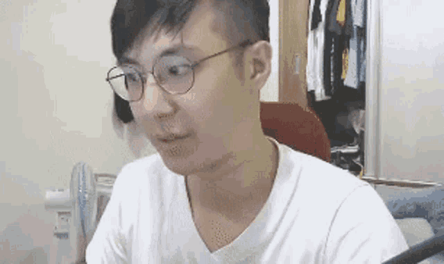 a man wearing glasses and a white shirt is sitting in front of a computer monitor .