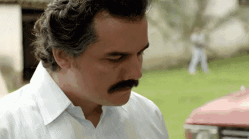 a man with a mustache and a white shirt is standing next to a red car .