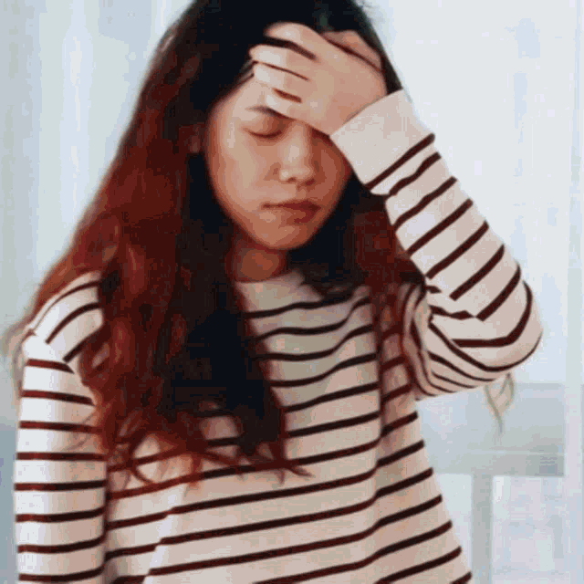 a woman in a striped shirt is holding her forehead