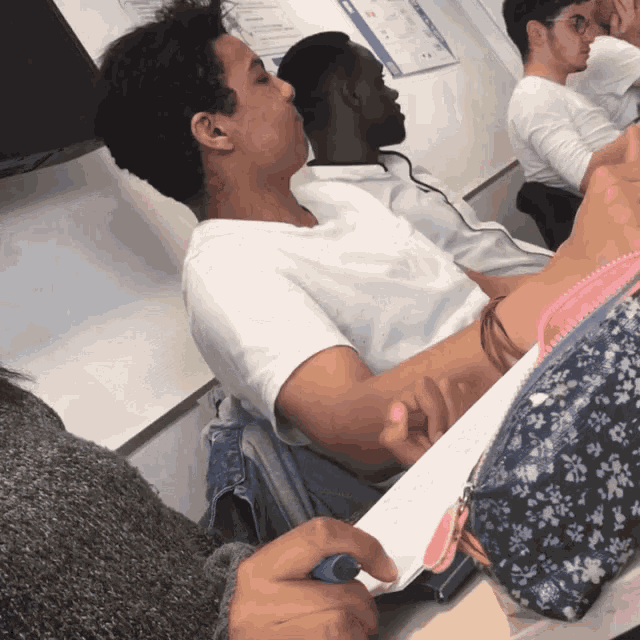 a man in a white shirt sits at a desk in a classroom with other students