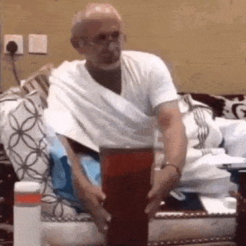 a man in a white shirt is sitting on a couch holding a large glass .