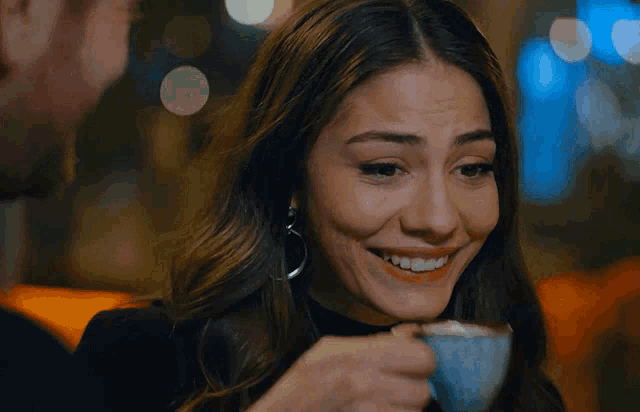 a woman drinking a cup of coffee with a man behind her