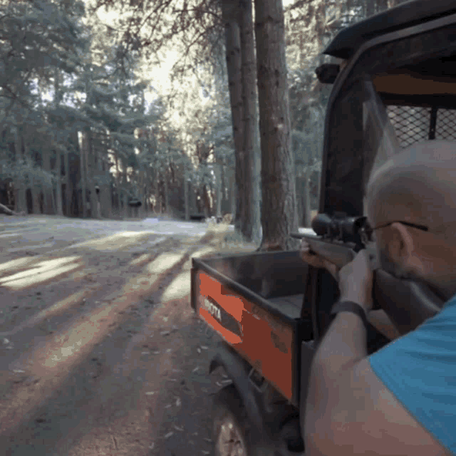 a man shooting a rifle from the back of a kubota utility vehicle