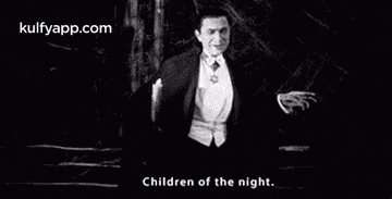 a black and white photo of a man in a tuxedo and bow tie standing in the dark .
