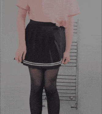 a woman in a pink shirt and black pleated skirt stands in front of a towel rack