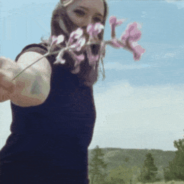 a woman in a black shirt is holding a pink flower