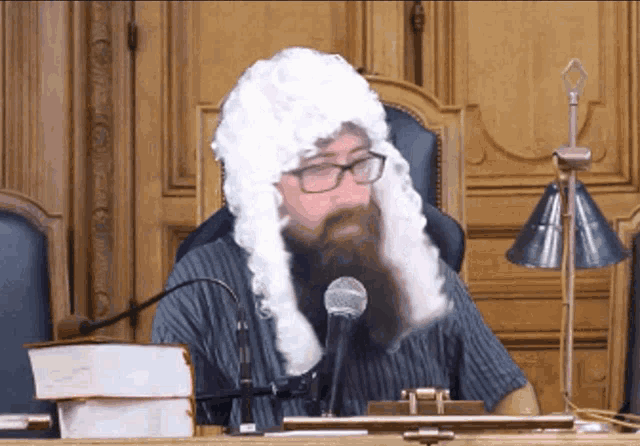 a man with a beard and a wig is sitting in front of a microphone in a courtroom