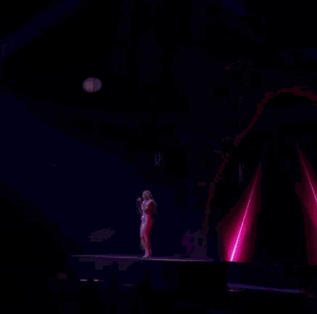 a woman singing into a microphone on a stage with purple lights