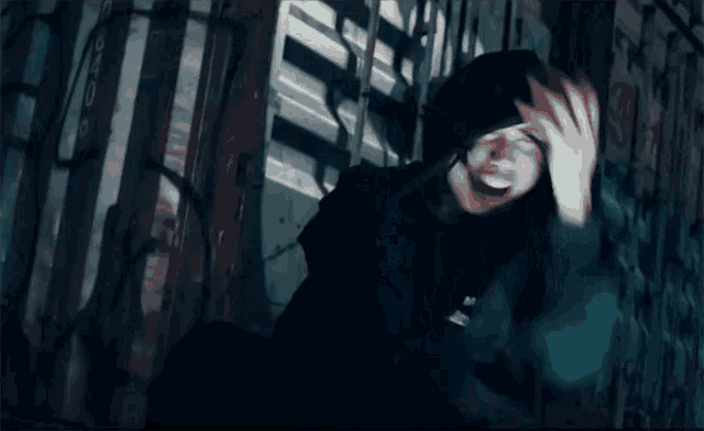a man in a hooded jacket is laughing in a dark room with graffiti on the wall