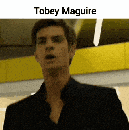 a man in a black suit is standing in front of a yellow wall with the name tobey maguire above him .