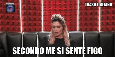 a woman is sitting on a couch in front of a red wall and says secondo me si sente figo