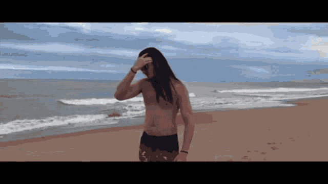 a shirtless man with long hair is standing on the beach