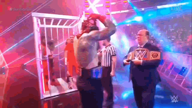 a wrestler is standing in a cage with a referee and holding a wrestling championship belt .
