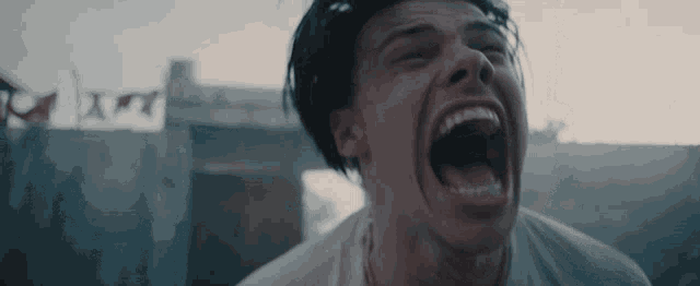 a close up of a man screaming with a few flags in the background