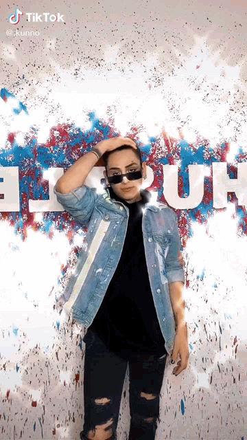 a man wearing sunglasses and a denim jacket stands in front of a wall that says tik tok