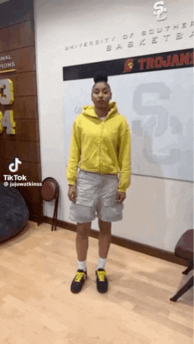 a woman wearing a yellow hoodie and shorts is standing in front of a white board .