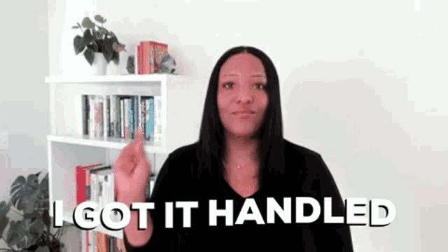 a woman is standing in front of a bookshelf and says `` i got it handled '' in sign language .