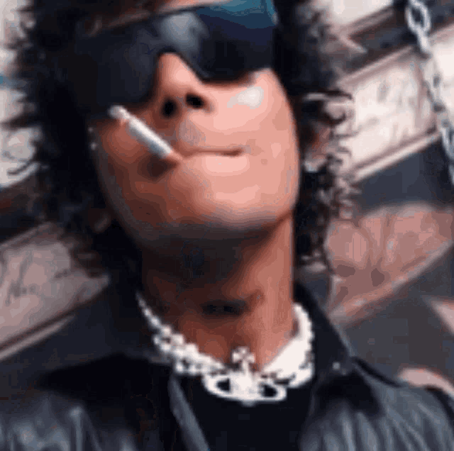a man wearing sunglasses and a chain around his neck smoking a cigarette